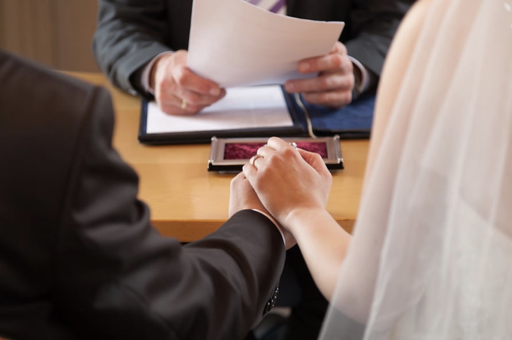 A couple holding hands in front of a person holding papers