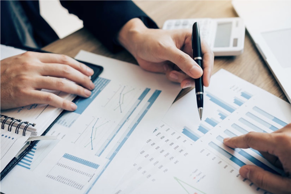 Closeup of paperwork with the hands of two people pointing at bar graphs