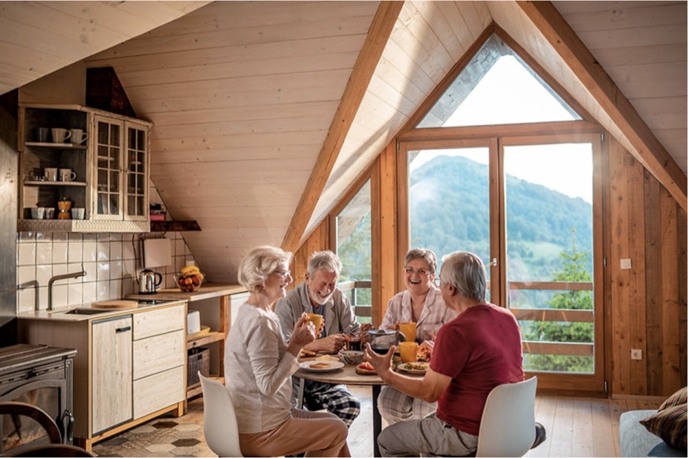 Group of four older people in a kitchen with a view of a forested mountain