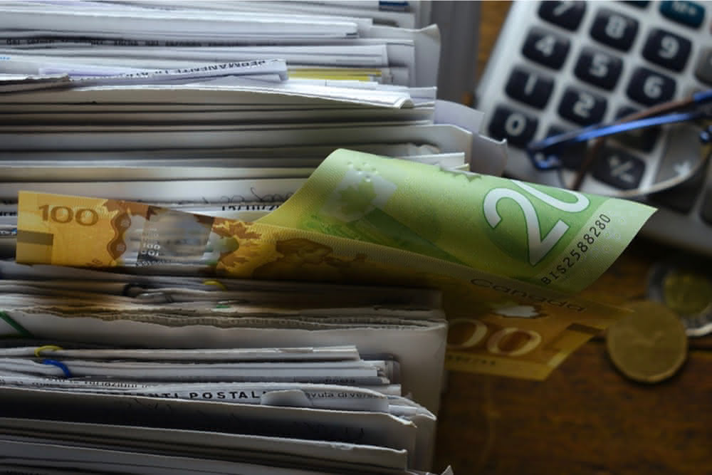 Stack of envelopes with some Canadian money showing with a calculator in the background